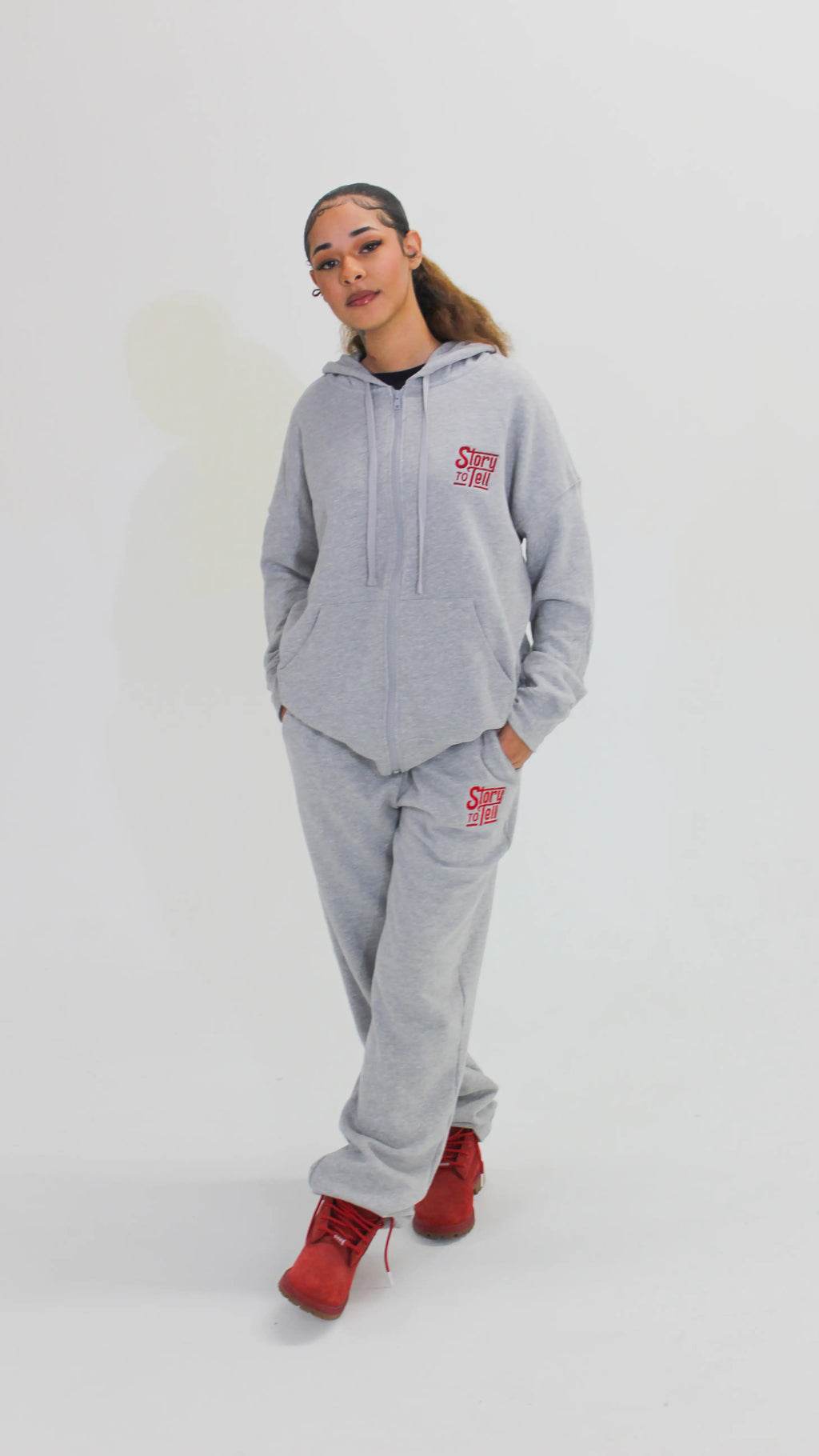 Person wearing a gray hoodie and pants with a red logo on a white background