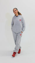 Person wearing a gray hoodie and pants with a red logo on a white background