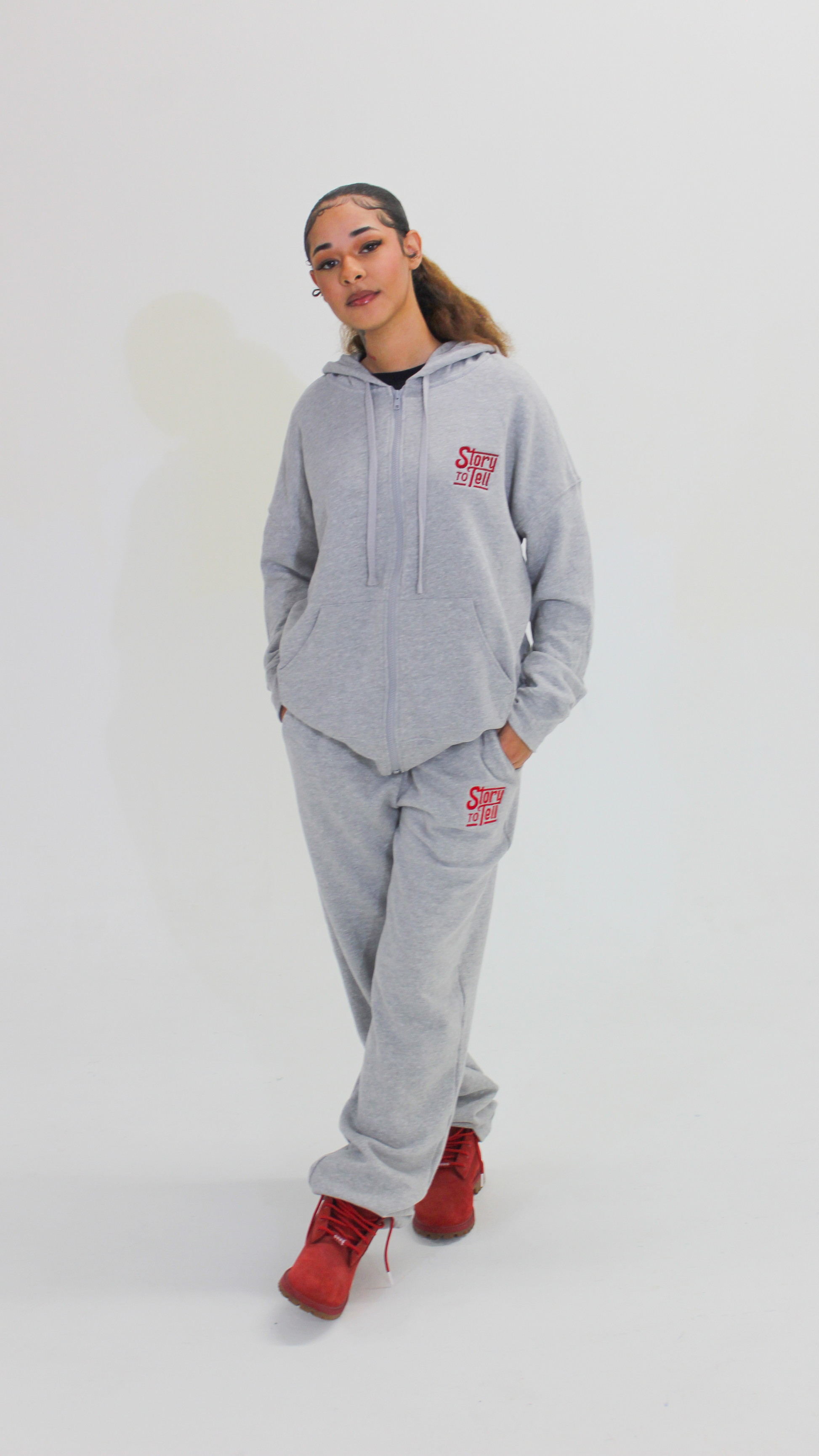 Person wearing a gray hoodie and pants with a red logo on a white background