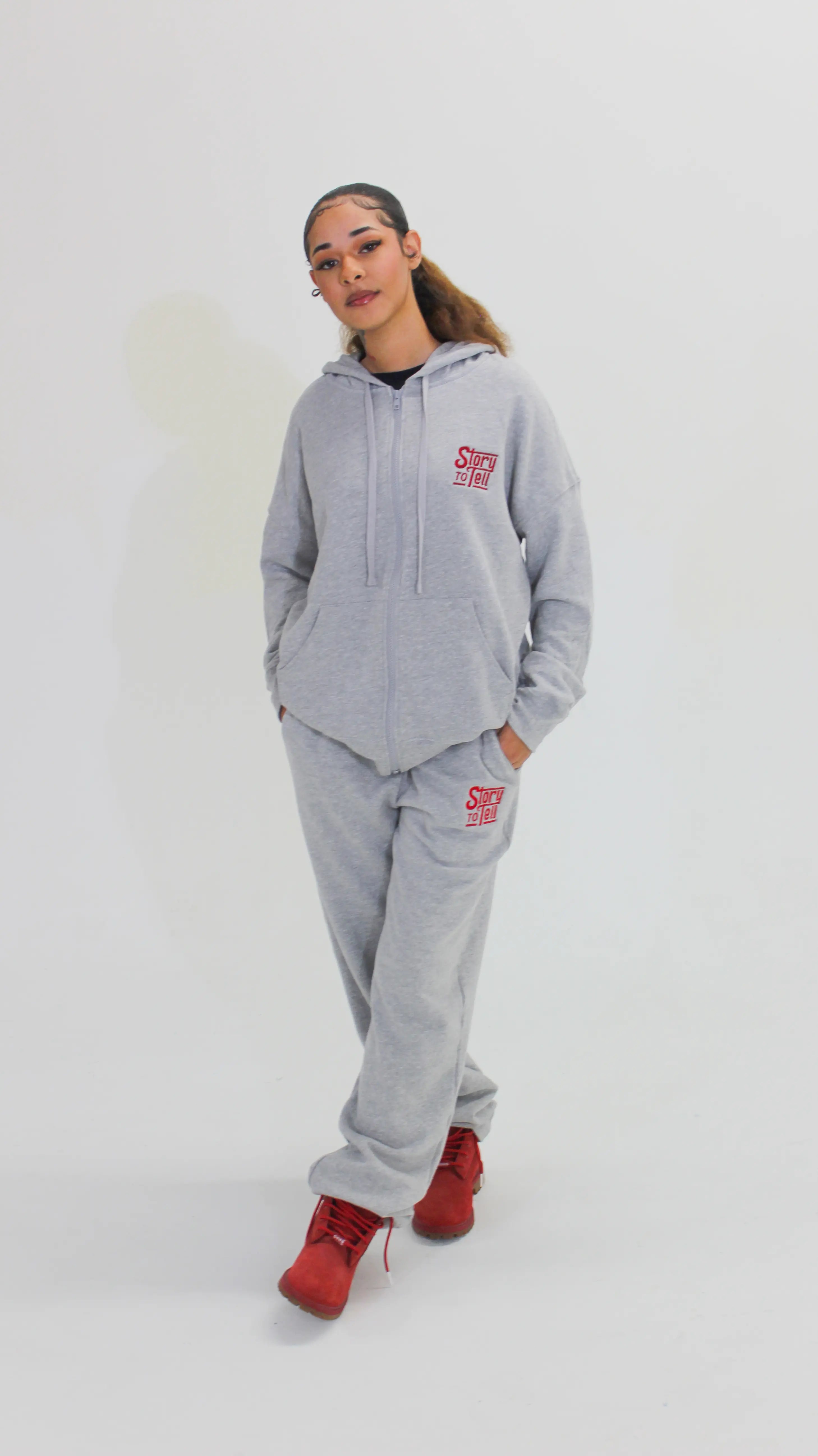 Person wearing a gray hoodie and pants with a red logo on a white background